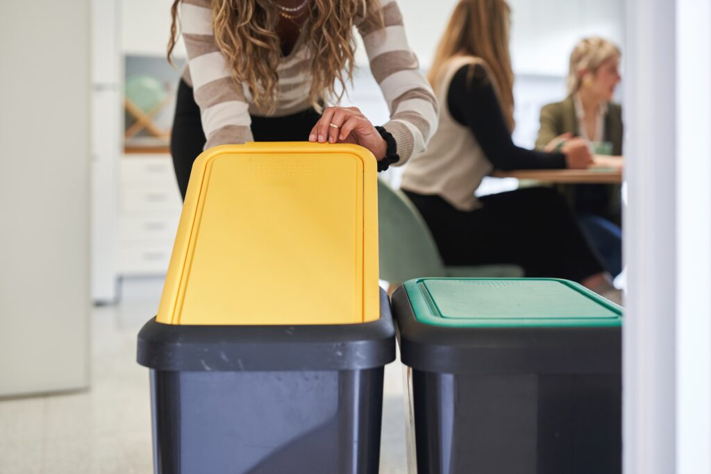 Woman recycling waste in office kitchen with color-coded bins